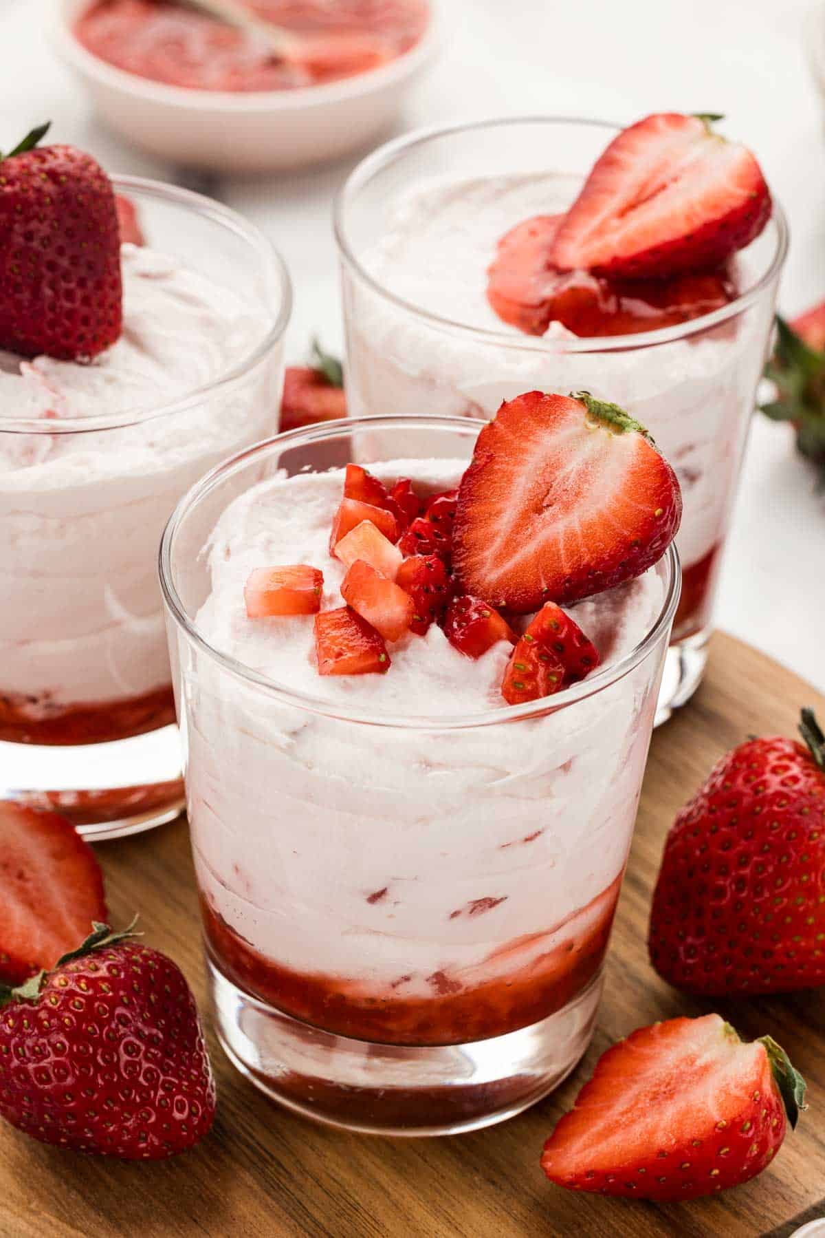 Chopped strawberries on top of a cup of mousse dessert.
