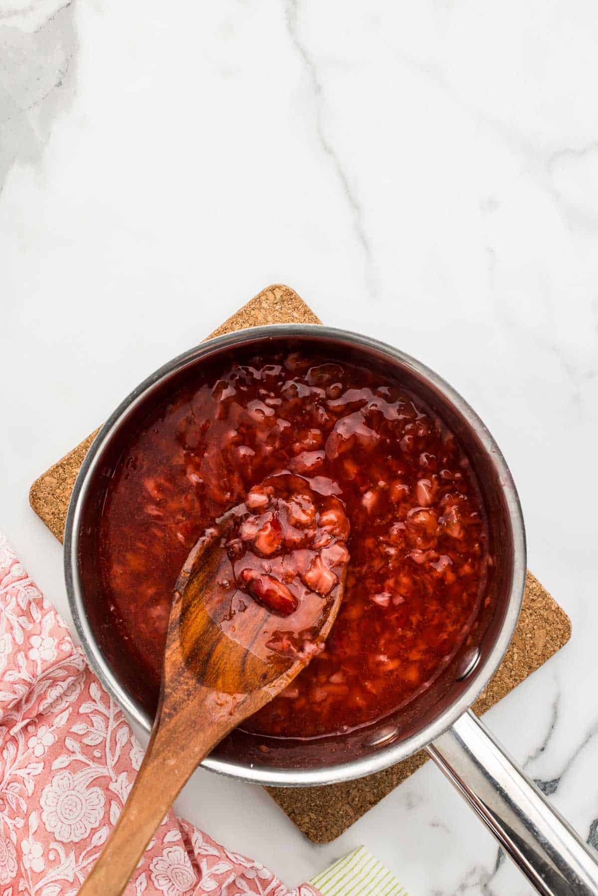 Strawberries cooked in a pan with a wooden spoon.