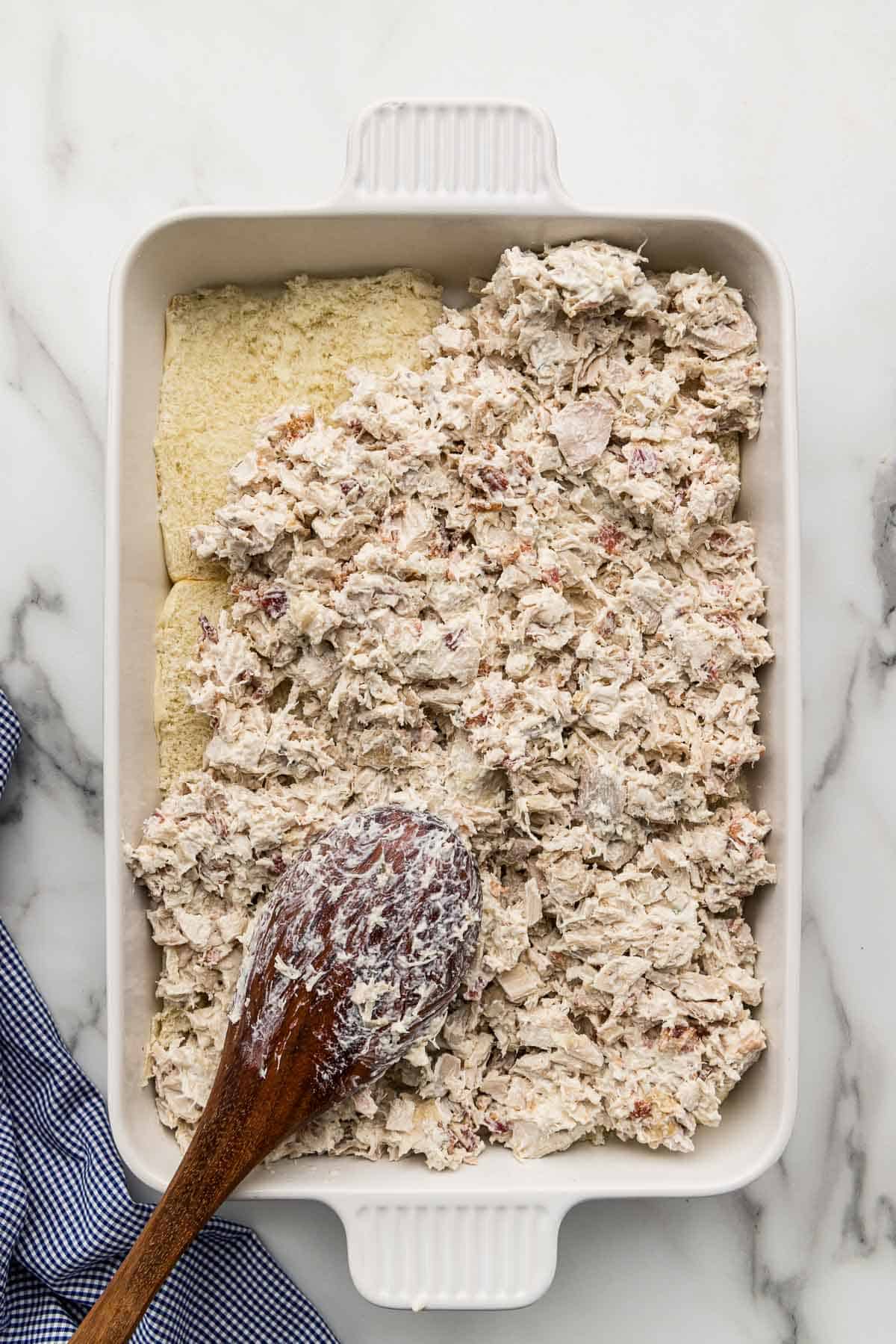 Chicken covered in ranch spread on bread in a baking pan with a spoon.