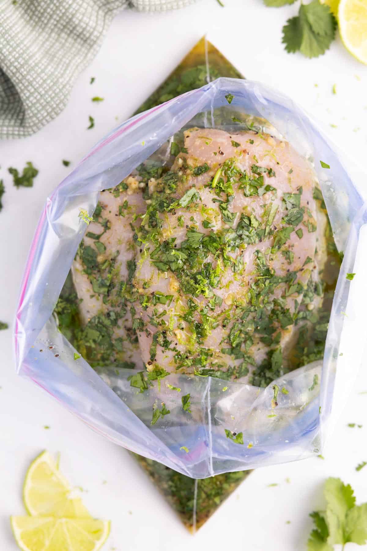 A ziplock bag with raw chicken sitting in marinade with herbs.