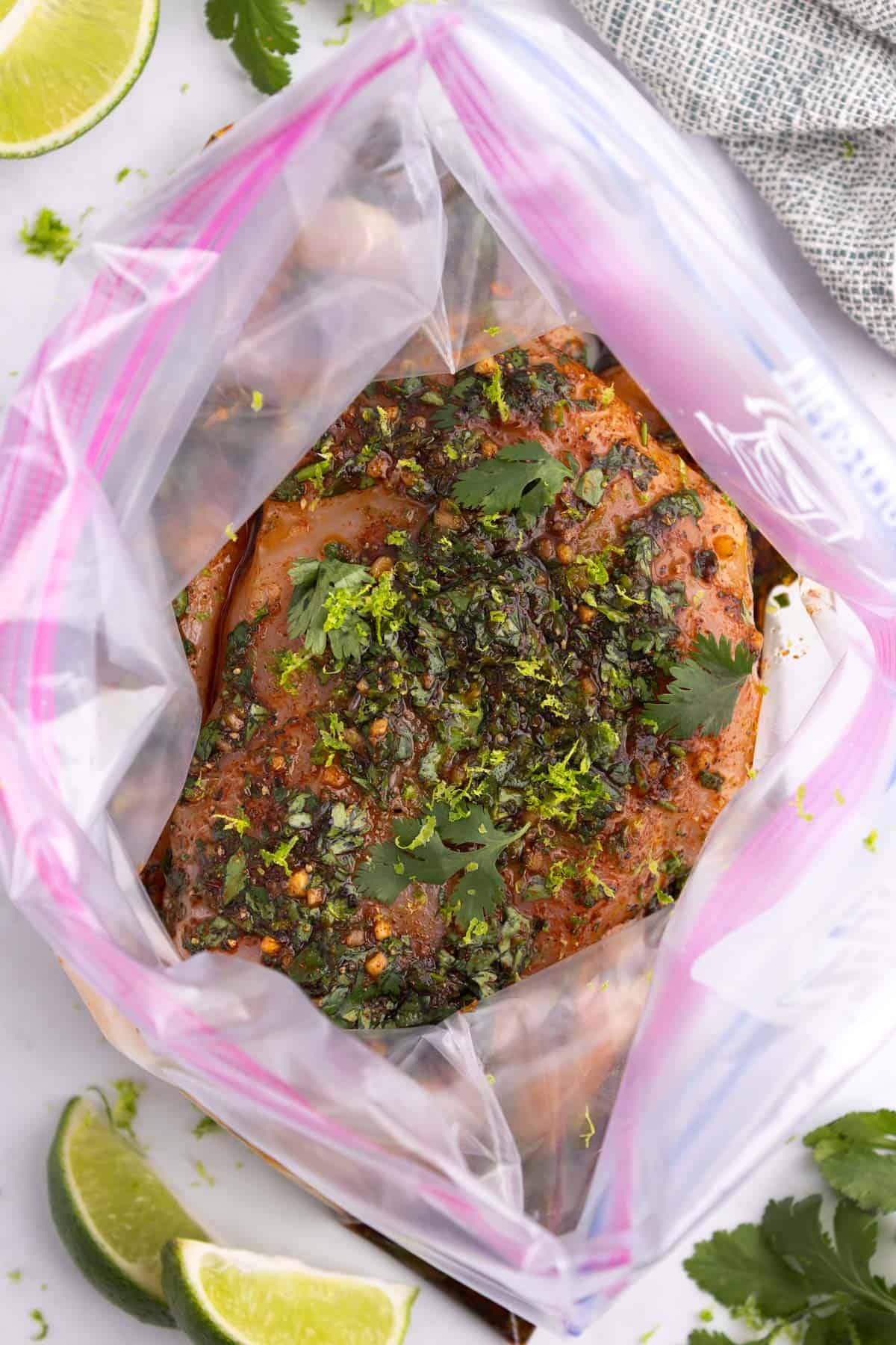 Chicken marinating in a ziplock bag topped with herbs.