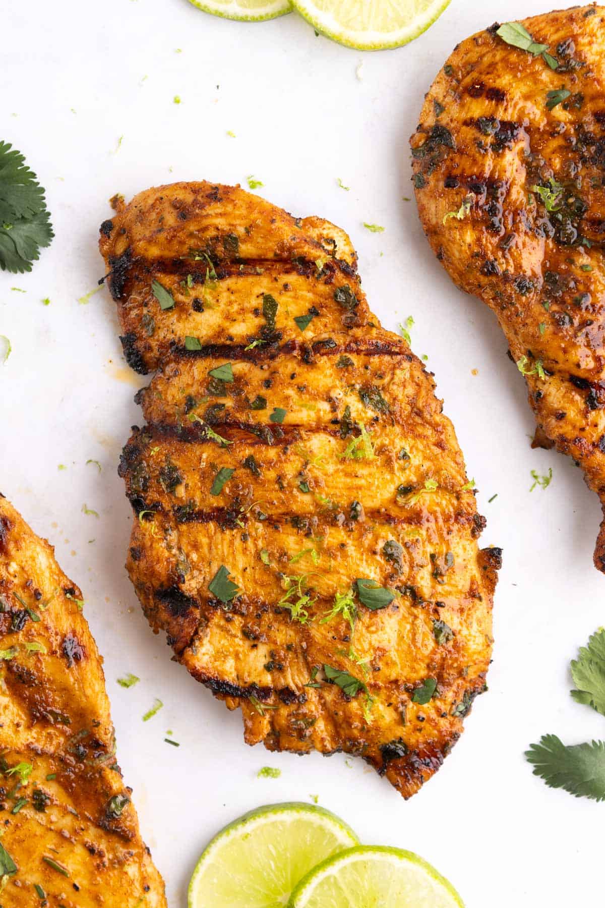 Three chicken breasts on a white surface with lime slices.