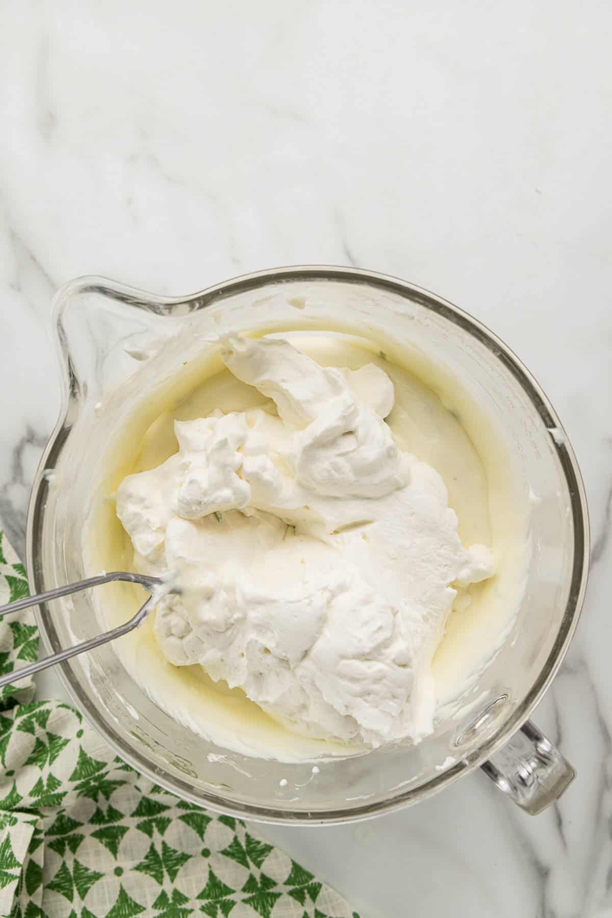Whipped cream being folded into a dish of ingredients with a spatula.