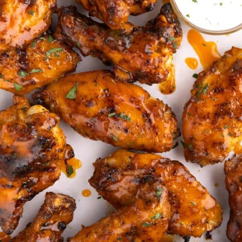 A pile of chicken wings on parchment with a small container of dip beside them.