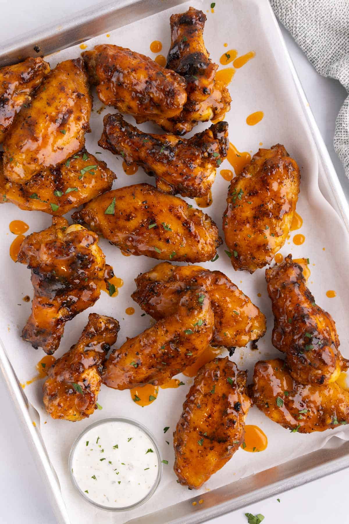 A cooking tray with grilled chicken wings and a small dish of dip.