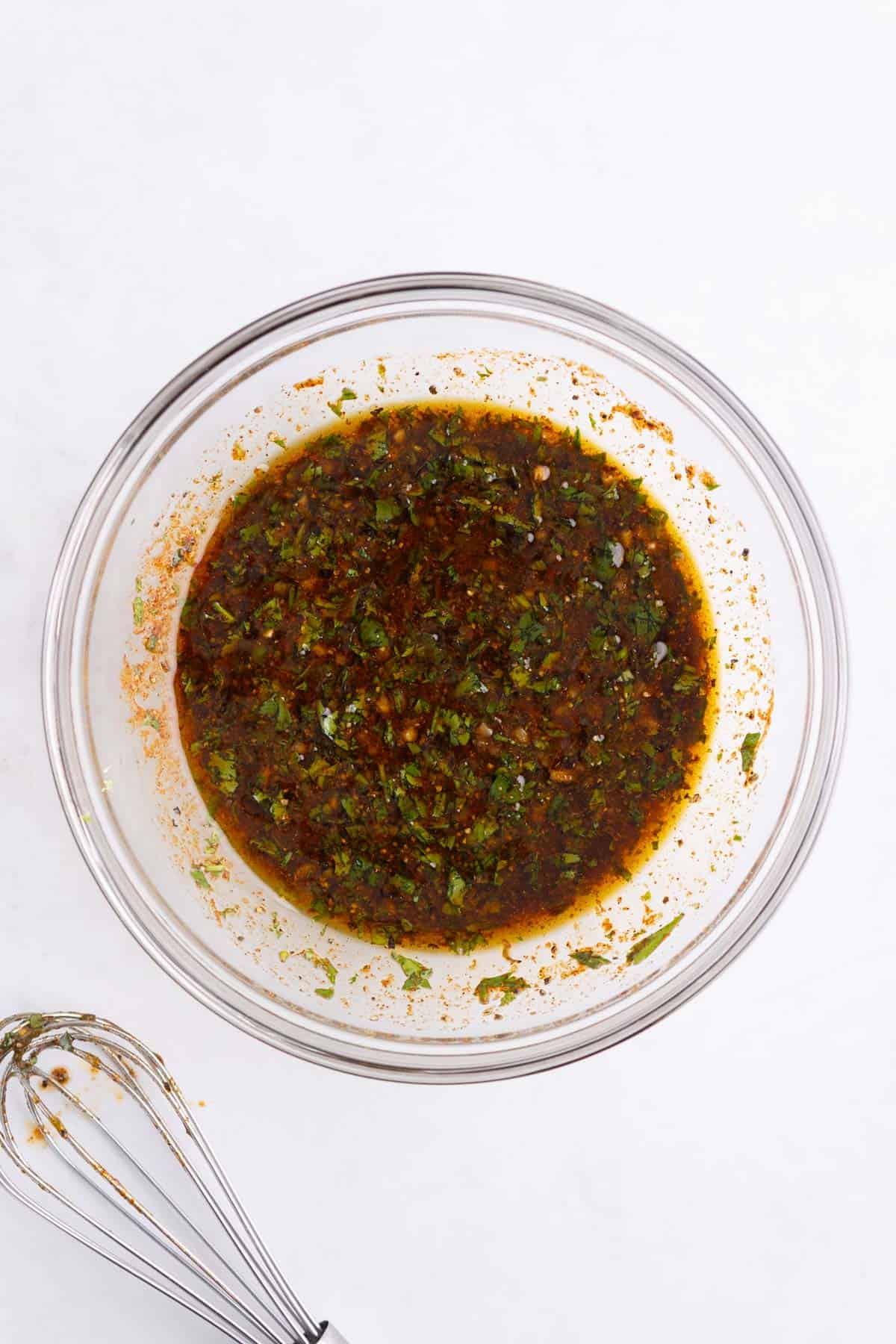 A glass bowl of chicken marinade mixed with a whisk.
