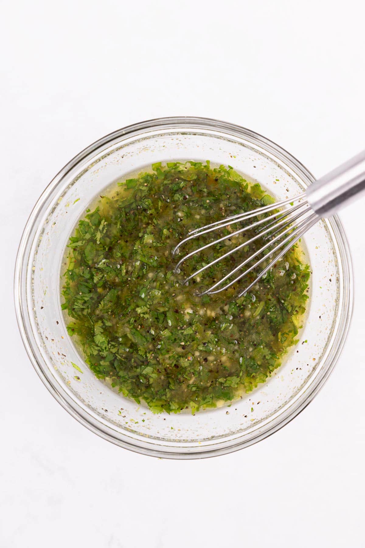 Cilantro lime marinade mixed in a glass bowl with a whisk.