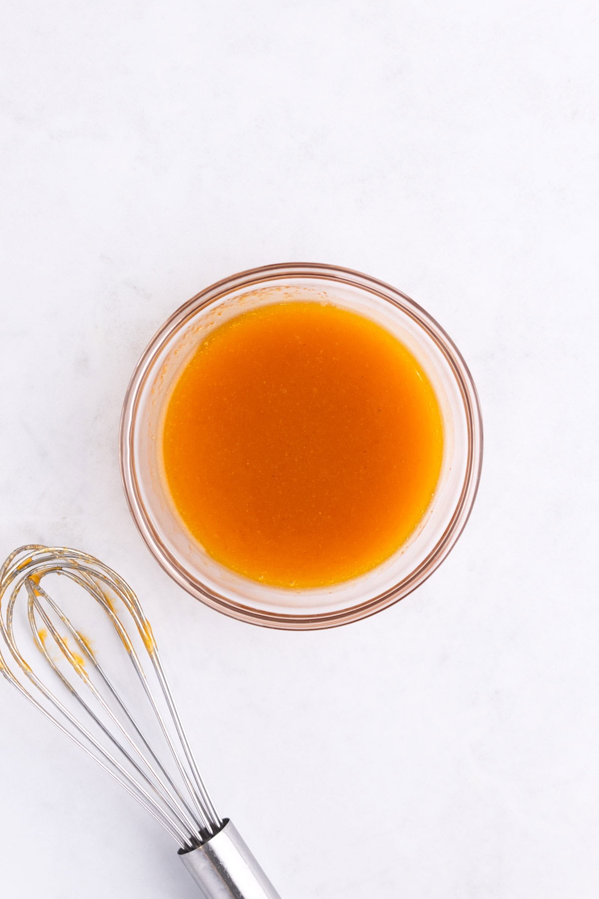 A small mixing bowl of honey buffalo sauce with a whisk.