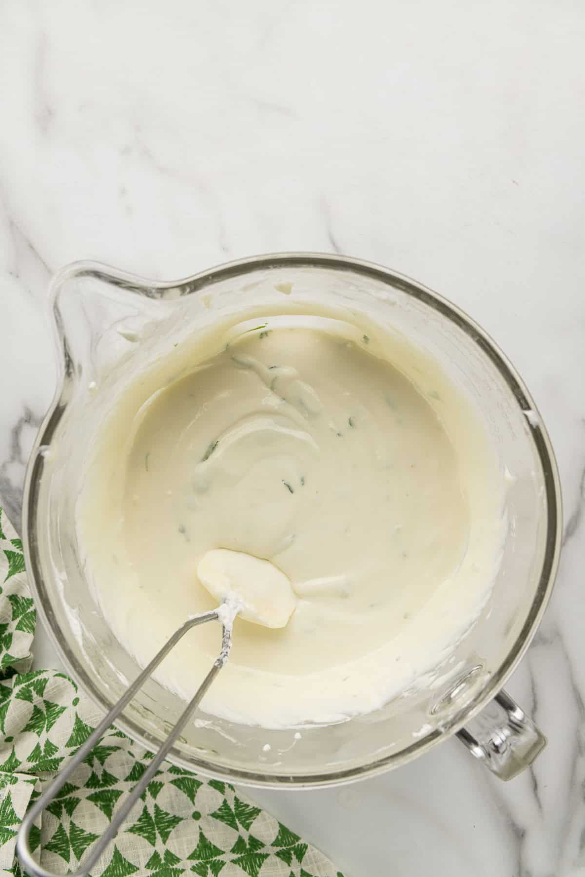 A measuring cup of lime cheesecake filling with a spatula.