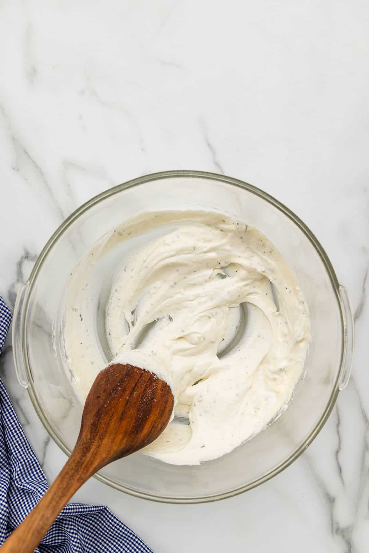 Ranch sauce mixed with a cooking spoon in a bowl.