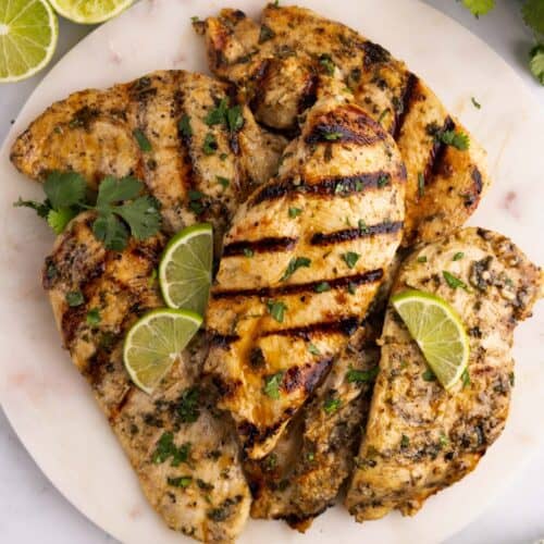 A large serving plate with grilled cilantro lime chicken breasts piled on it.