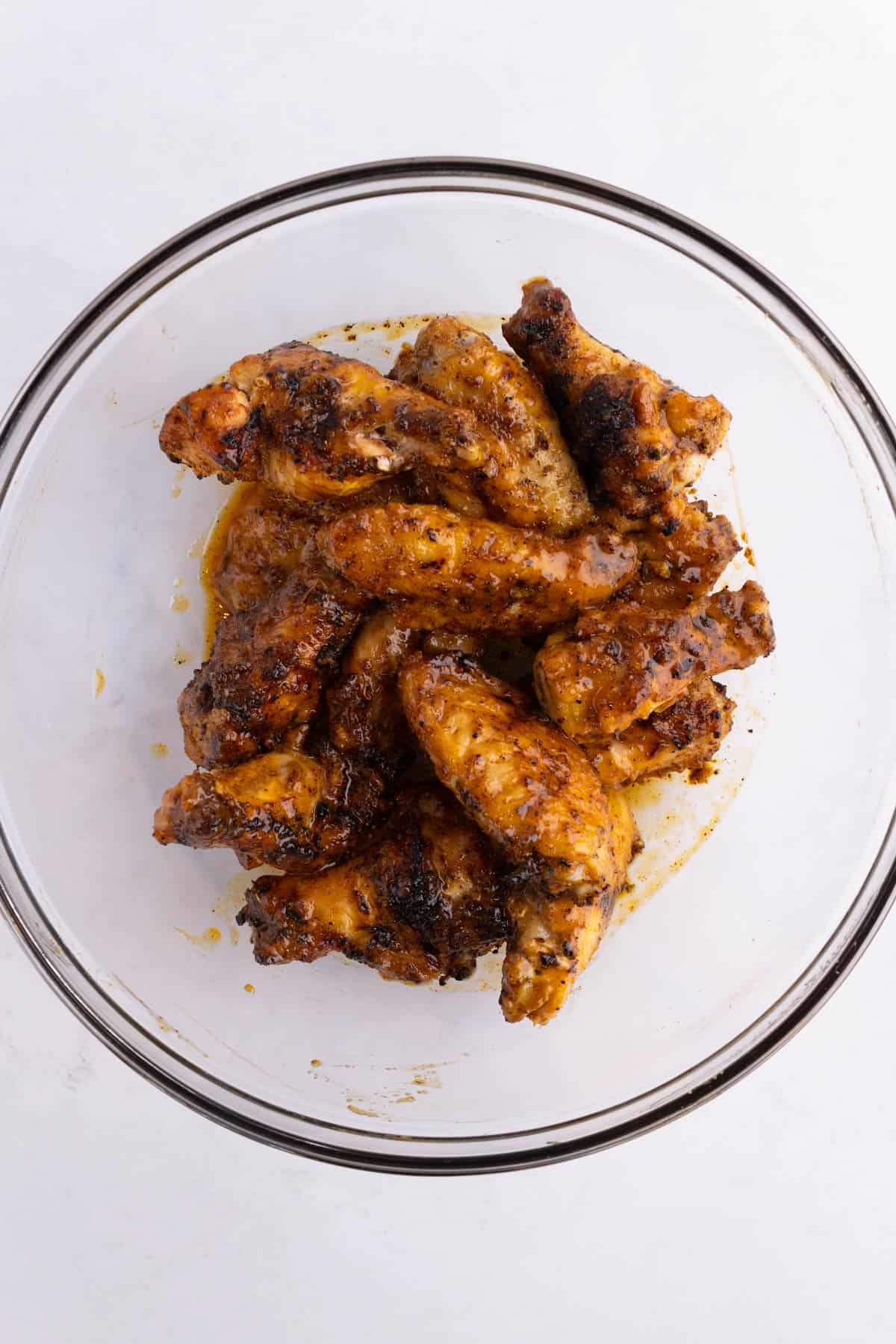 Wings covered in BBQ sauce in a mixing bowl.