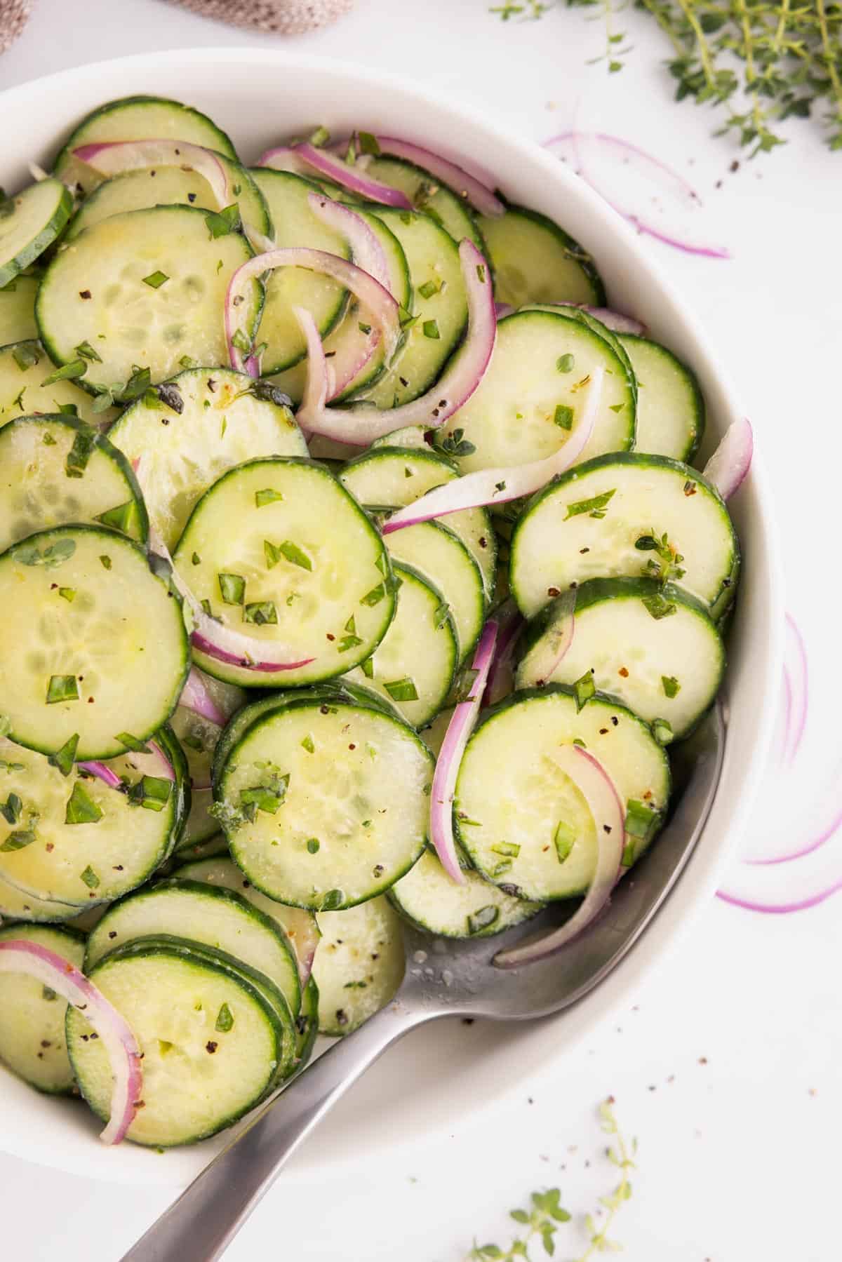 Cucumber salad with honey dijon dressing in a serving bowl with a spoon.
