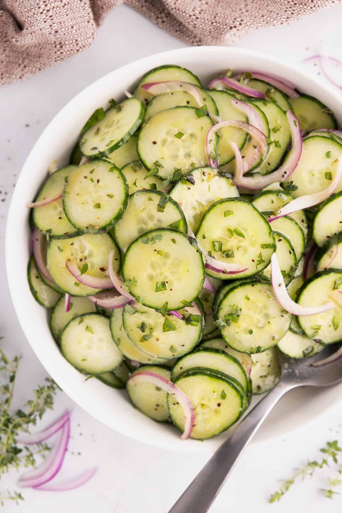 Cucumber salad piled into a white bowl with silverware.