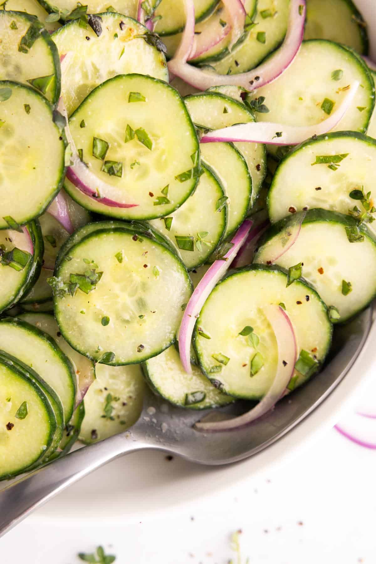 CLoseup of a spoon tucked into a bowl of cucumber salad.