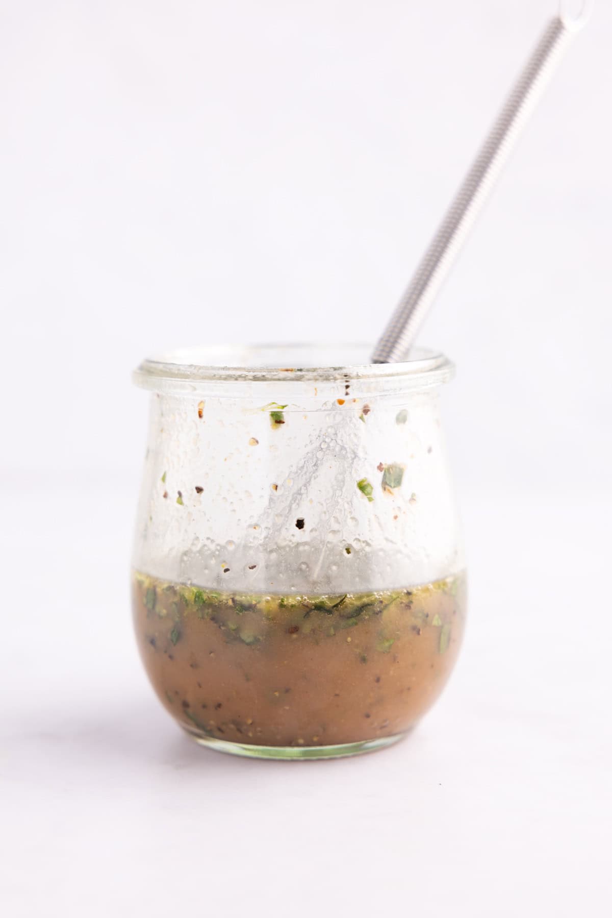 A jar of salad dressing with a small whisk dipped into it.