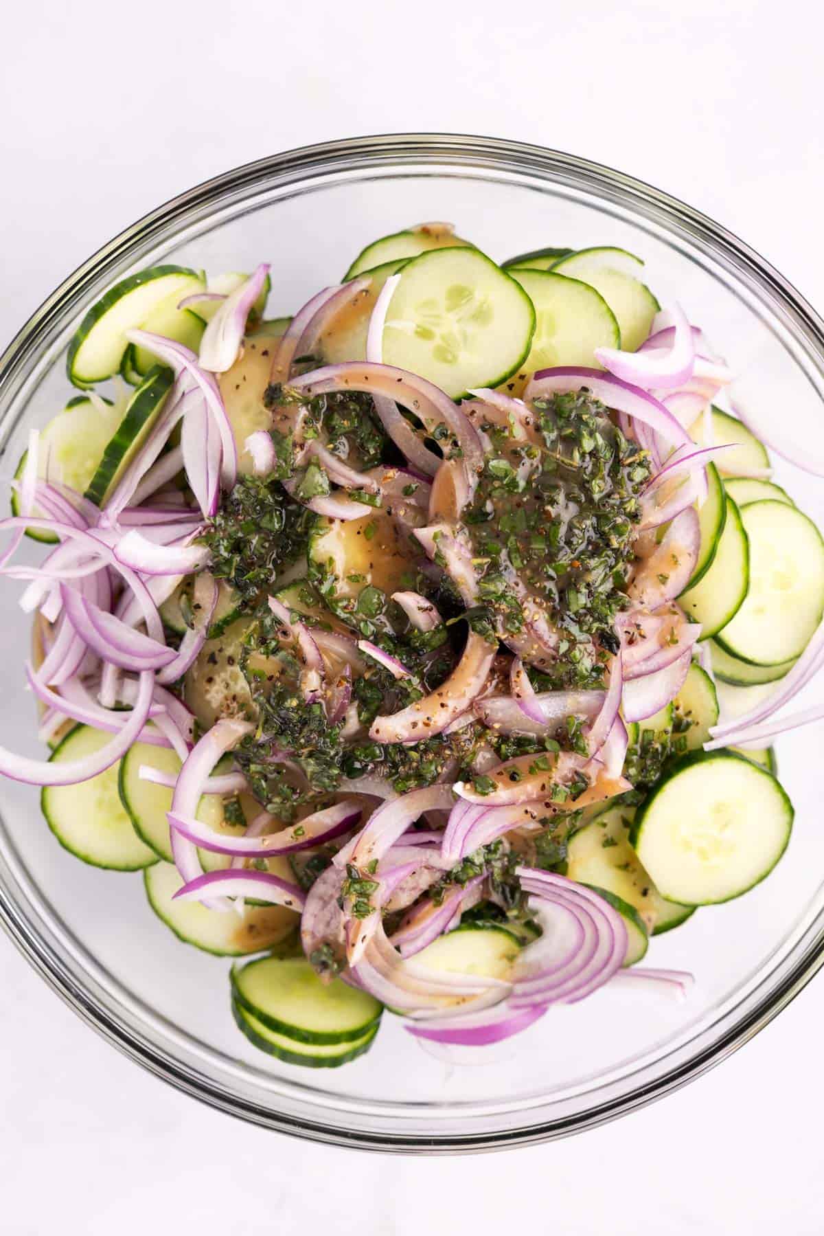 A large bowl full of cucumbers, onion, and dressing unmixed.