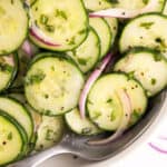 Sliced cucumbers drenched in dressing with a spoon.