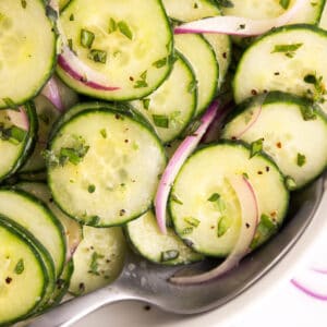 Sliced cucumbers drenched in dressing with a spoon.
