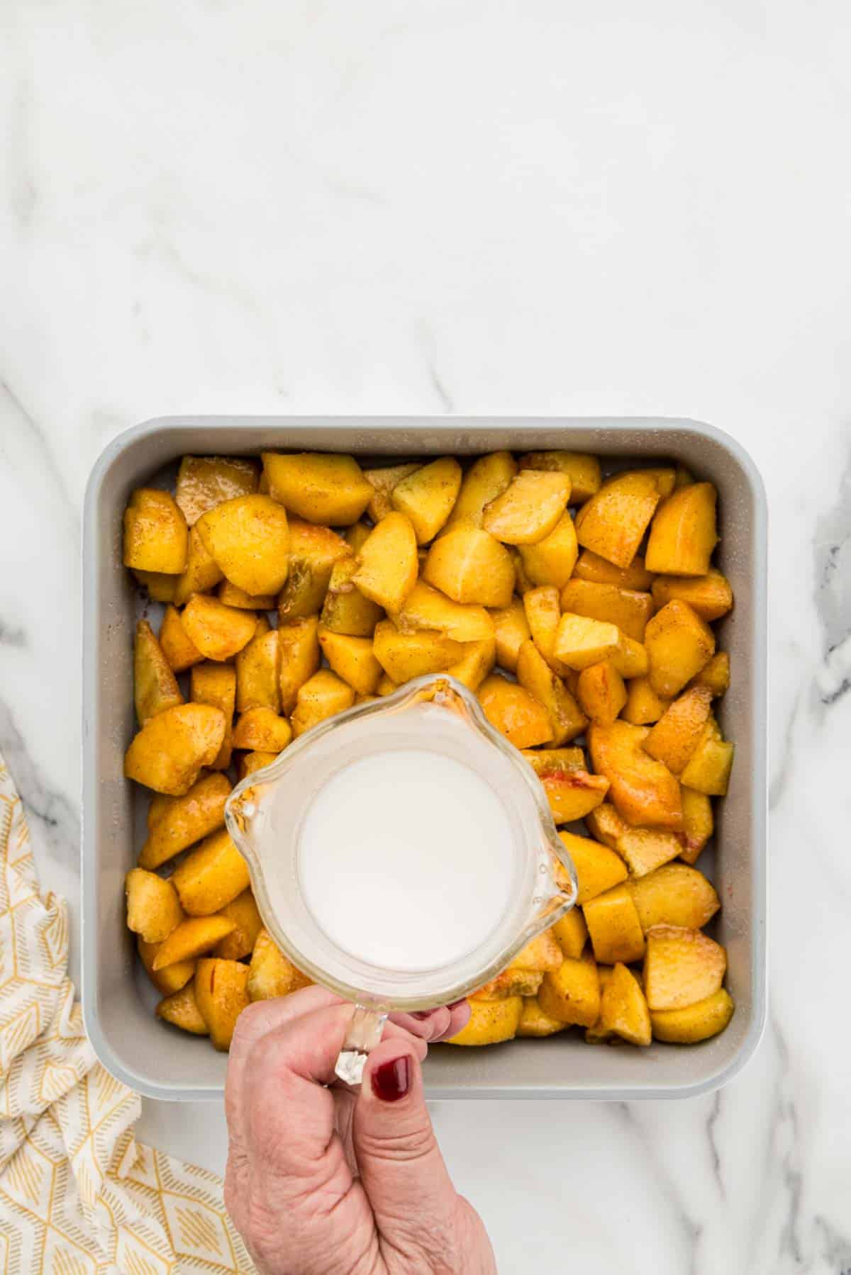 Pouring cornstarch on a pan of cut peaches.