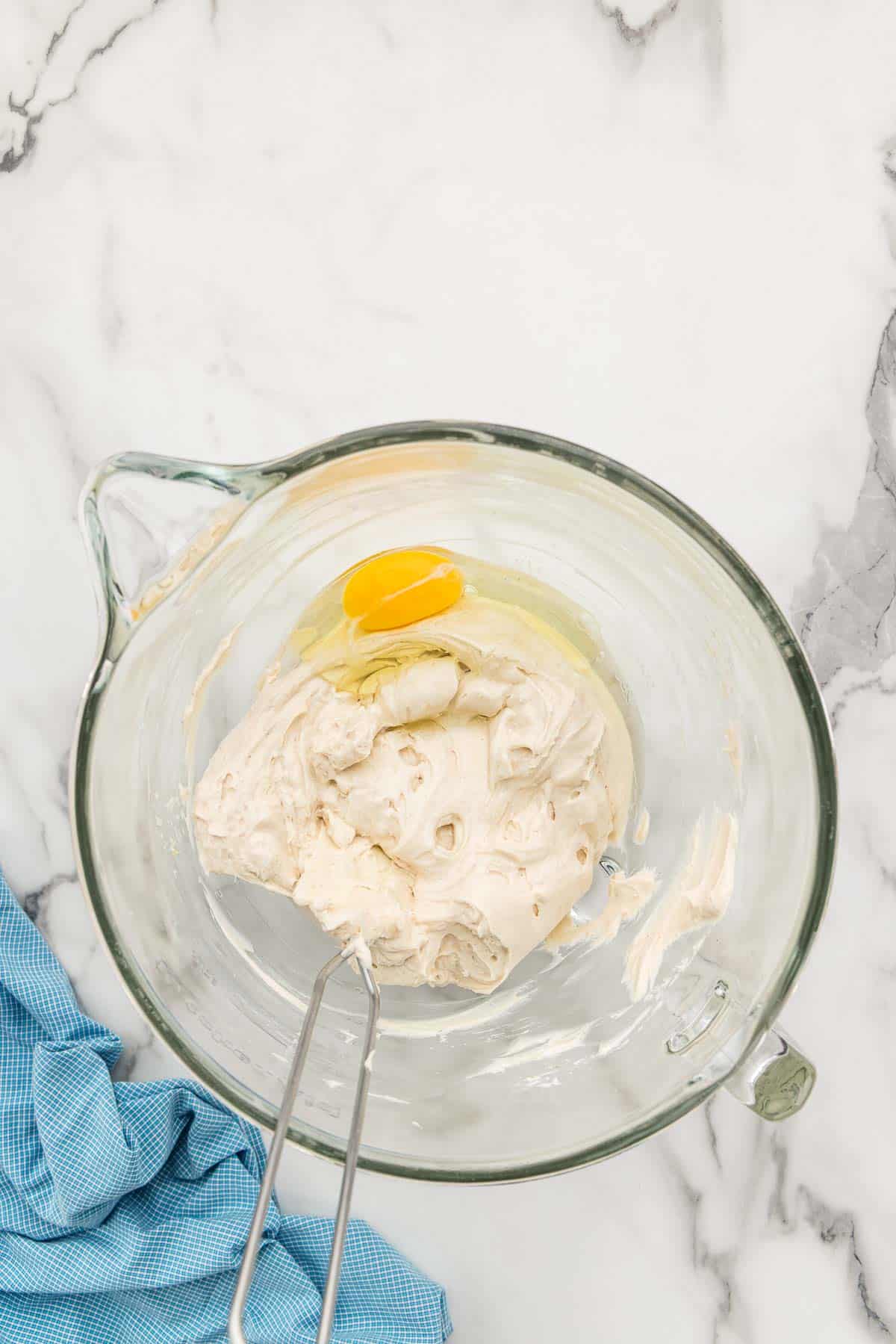 Eggs added into cheesecake batter in a glass measuring cup with a spatula.