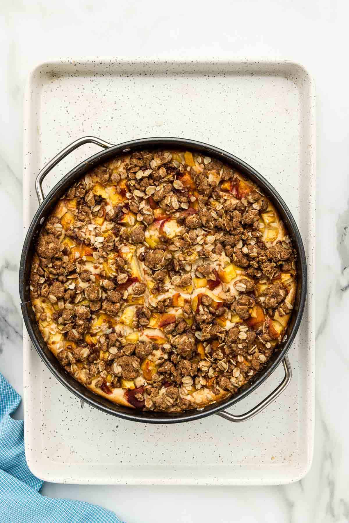 Baked peach cheesecake in a pan with crumble topping.
