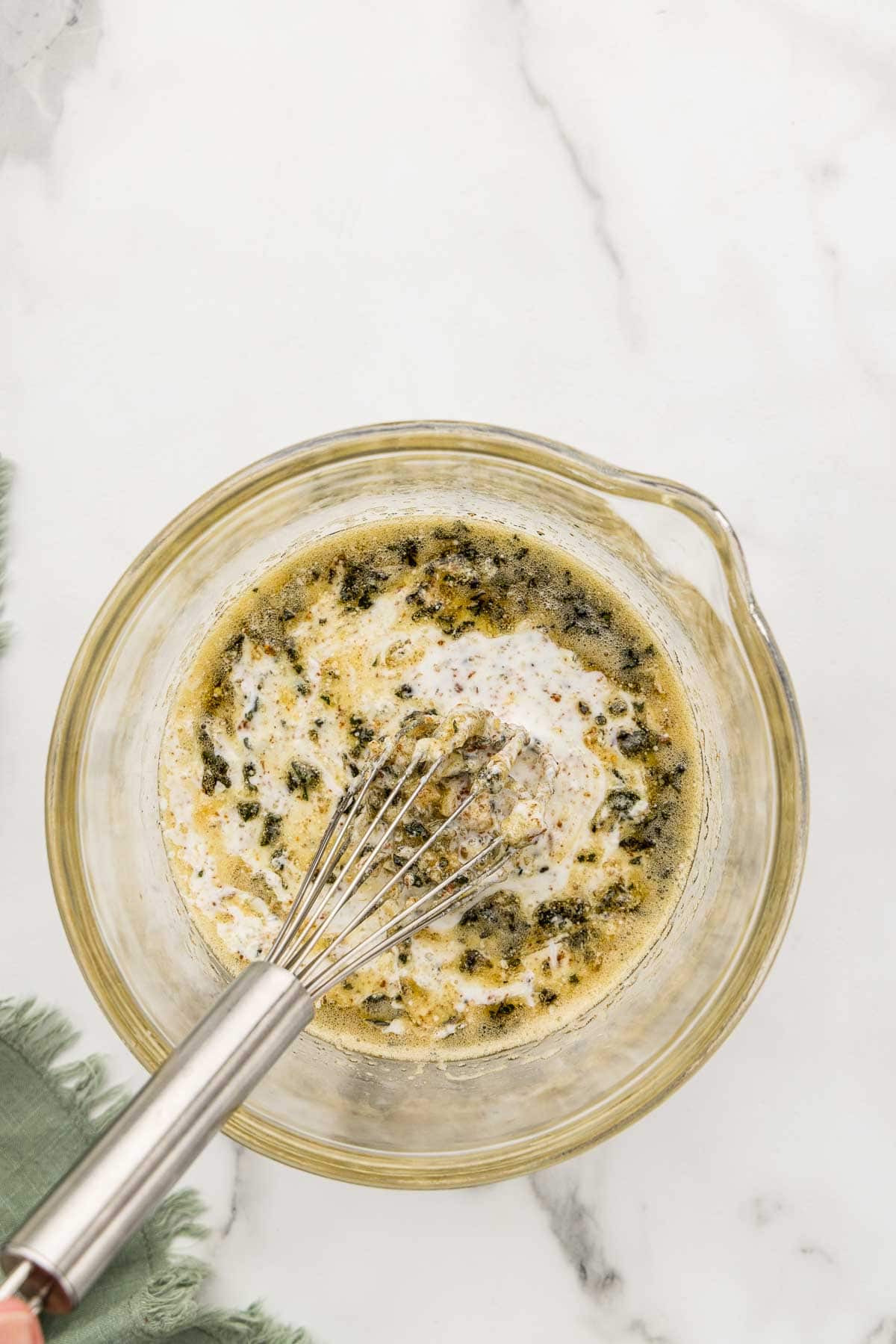 Sage added to dough in a glass cup with a whisk.