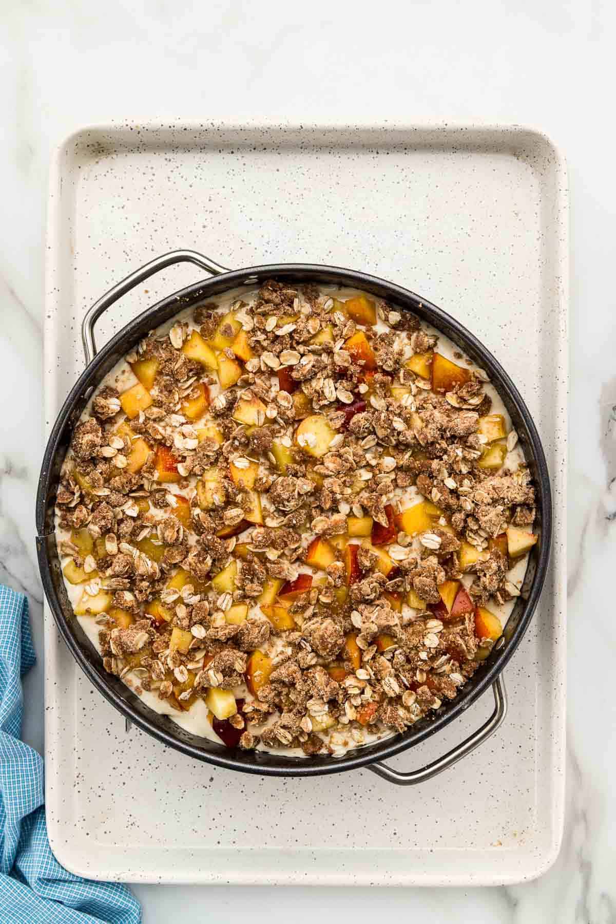 Topping added to a pan of cheesecake with peaches.