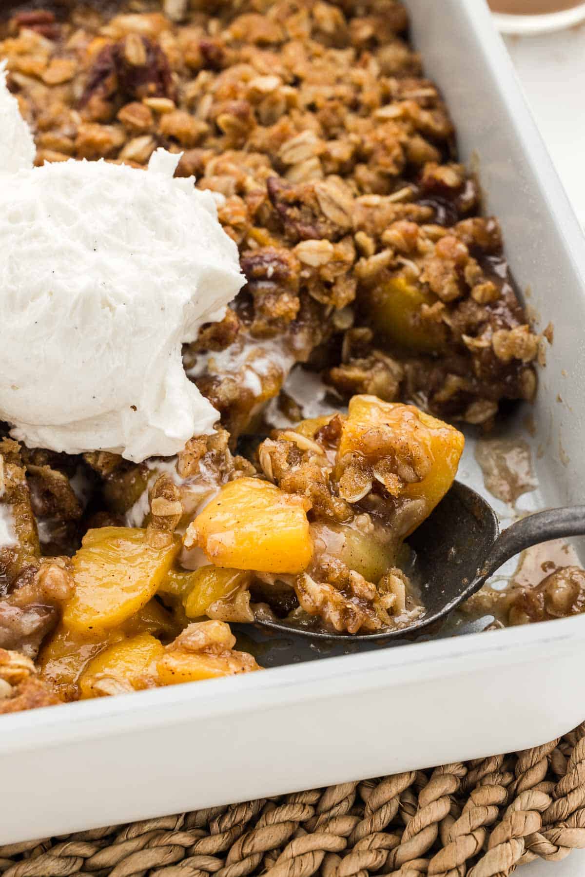 A spoonful of peach crisp taken in a pan with a scoop of ice cream.