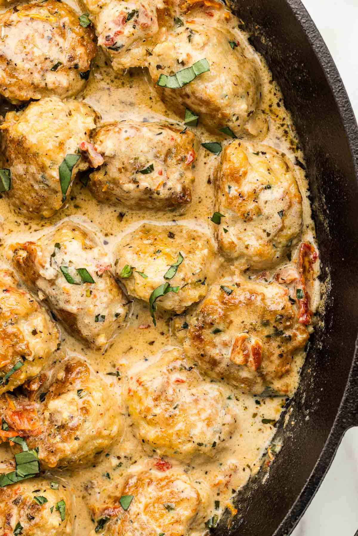 CLoseup of chicken meatballs covered in sauce in a cast iron pan.