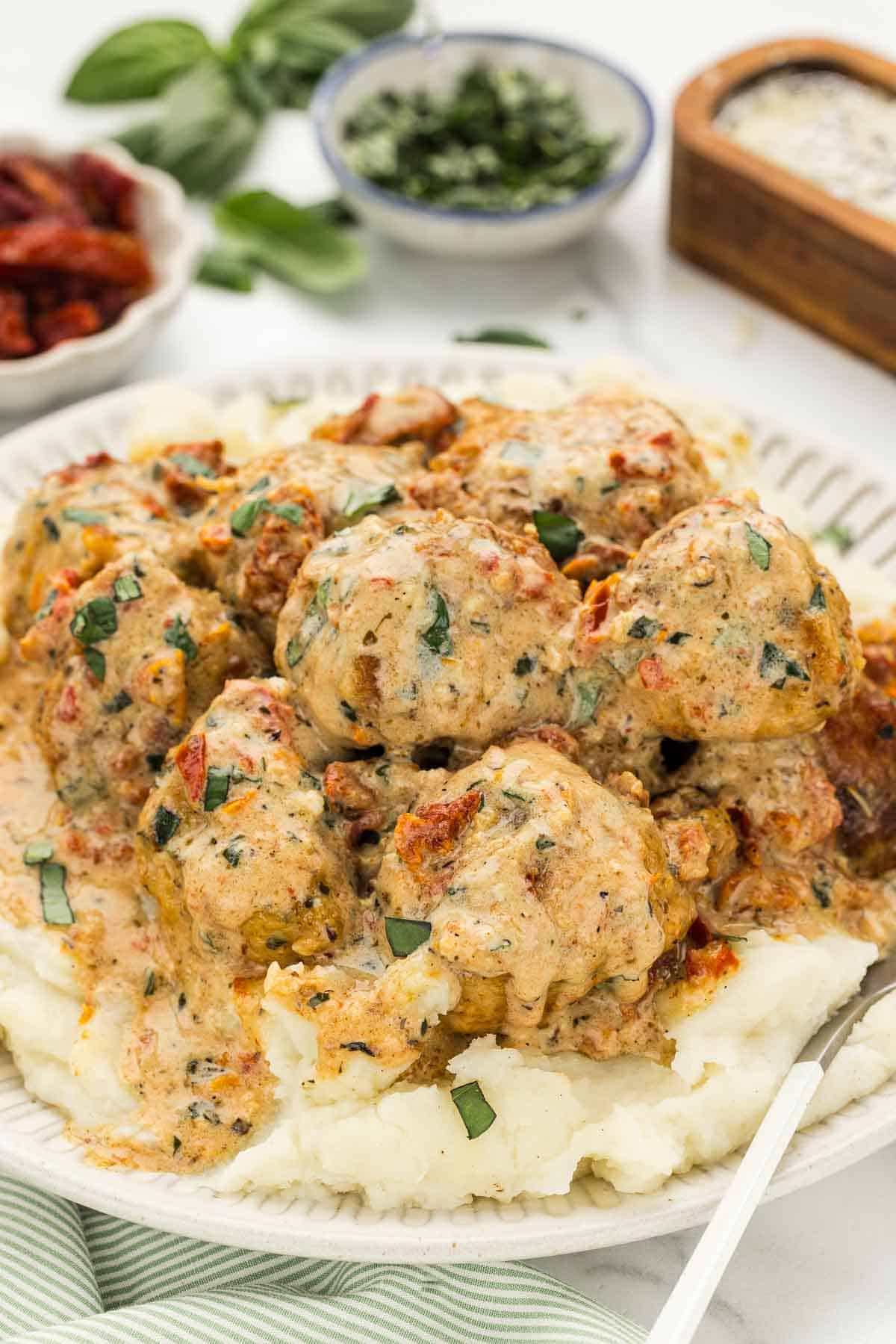 A stack of marry me chicken meatballs over potatoes on a plate.