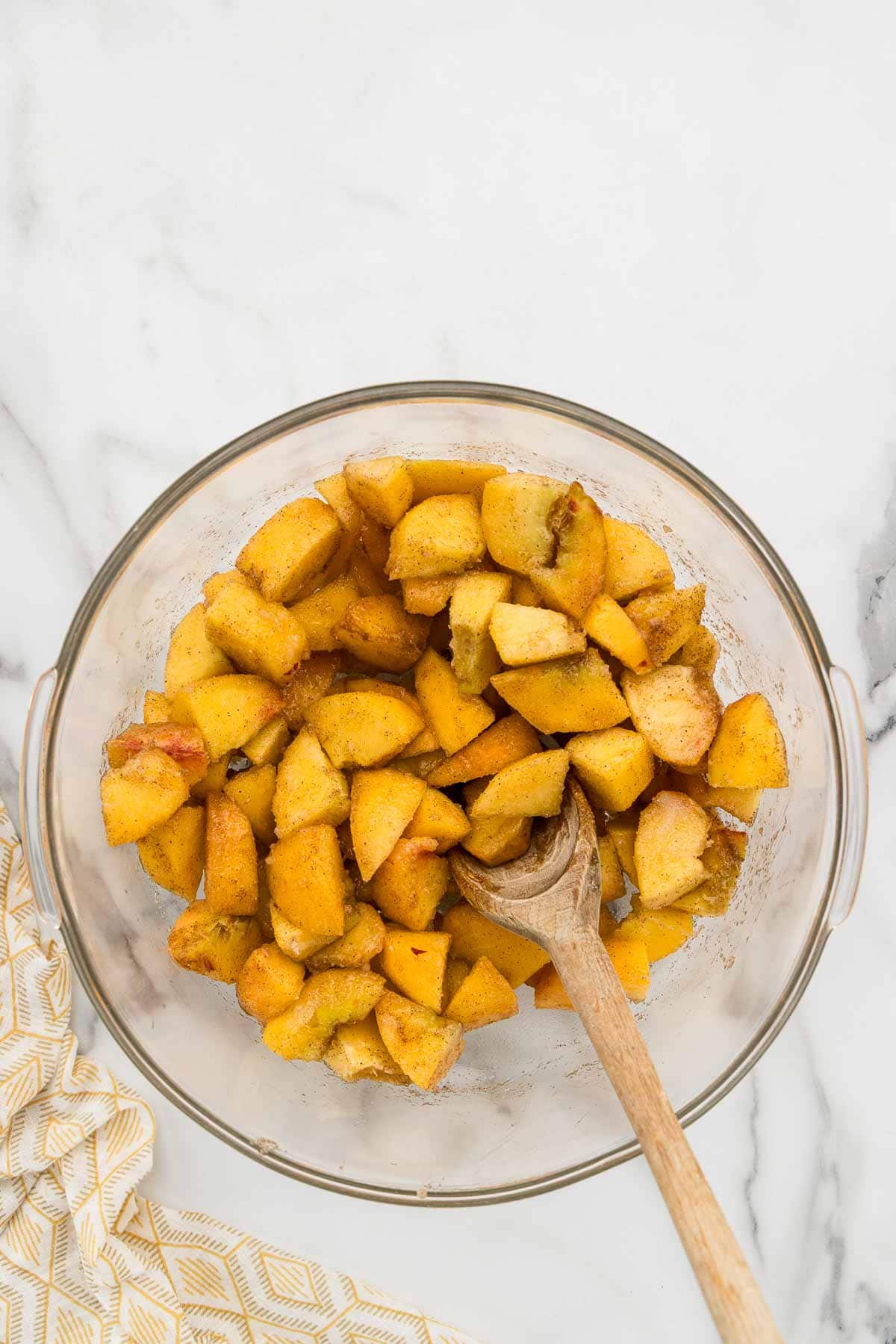 Sweet and juicy peaches in a glass bowl with a wooden spoon.