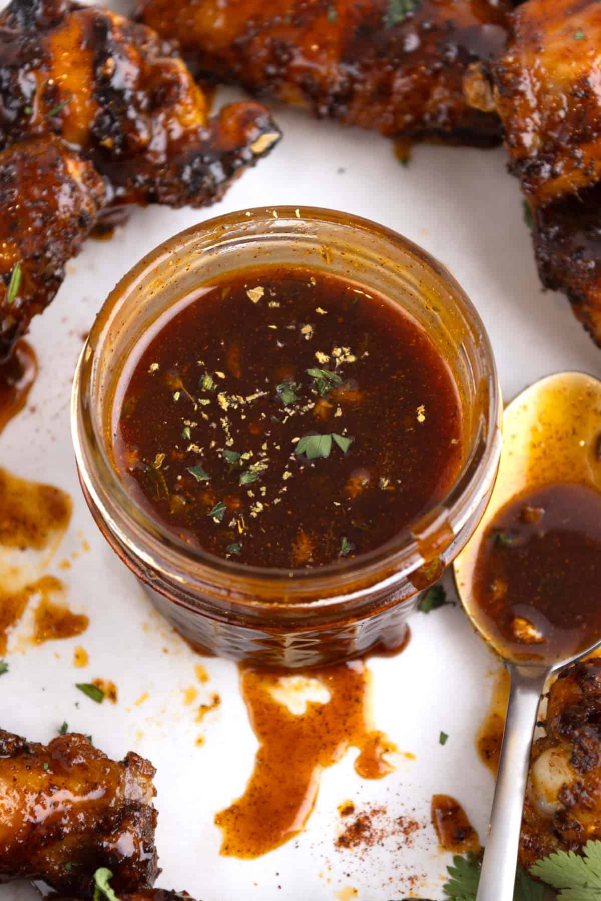 A jar of sauce in the middle of an array of chicken wings.