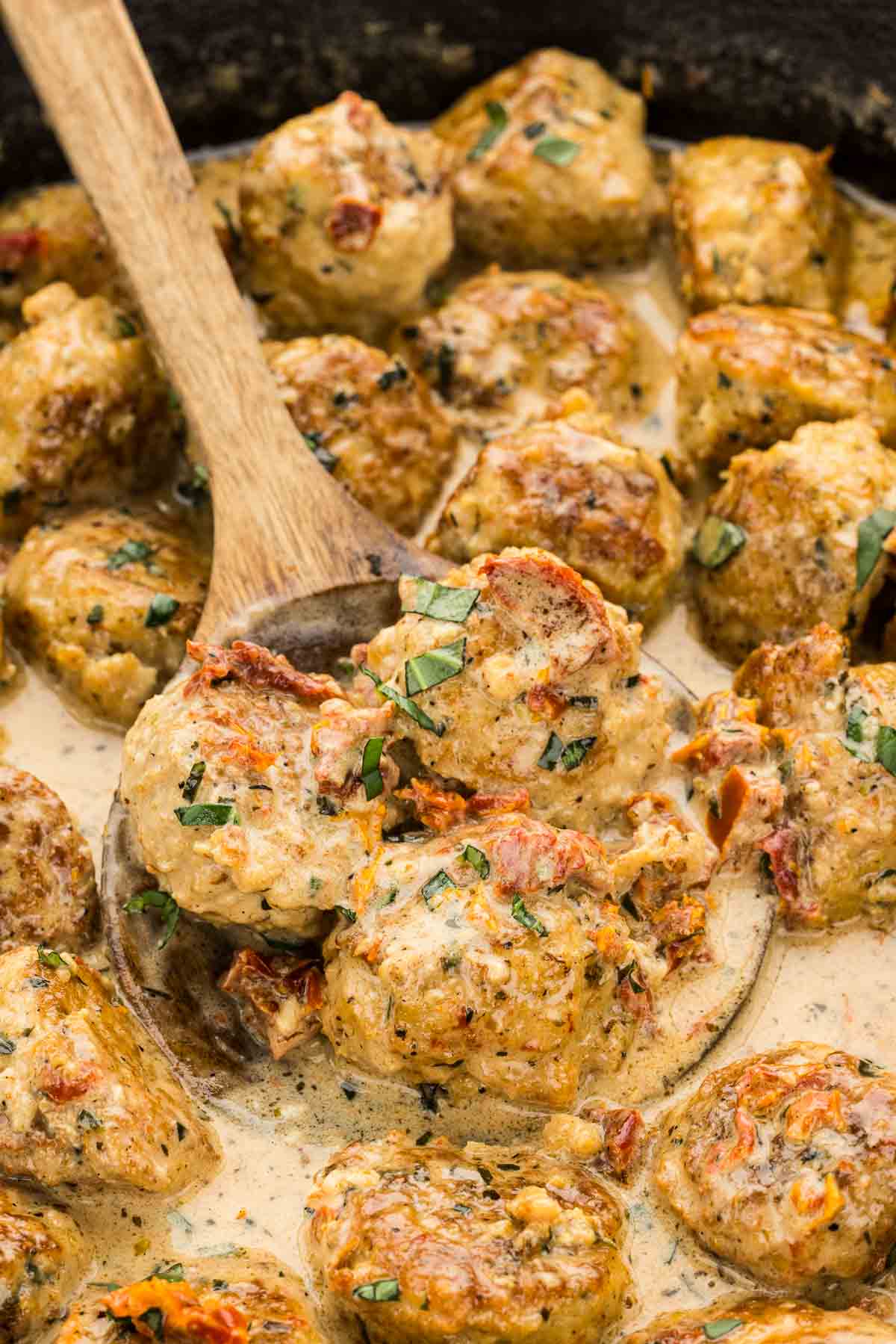 A wooden cooking spoon holding marry me chicken meatballs.