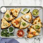 A large pan of crispy quesadillas with an array of toppings around them.