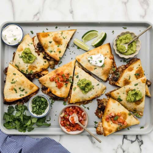 A large pan of crispy quesadillas with an array of toppings around them.