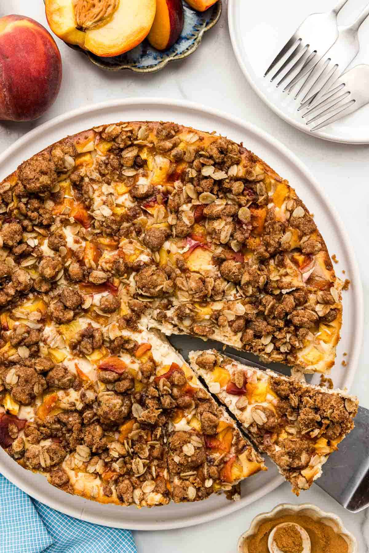 A serving spatula taking a slice of out of a whole peach cheesecake on a platter.