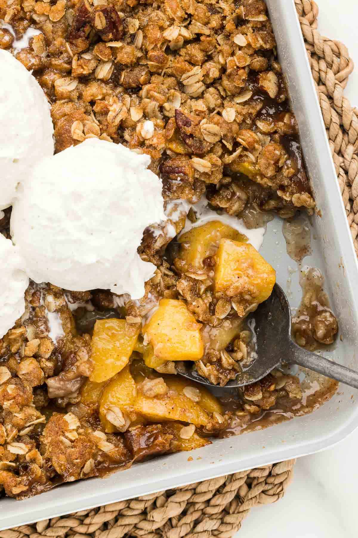 The corner of a baking pan full of peach crisp with a spoon.