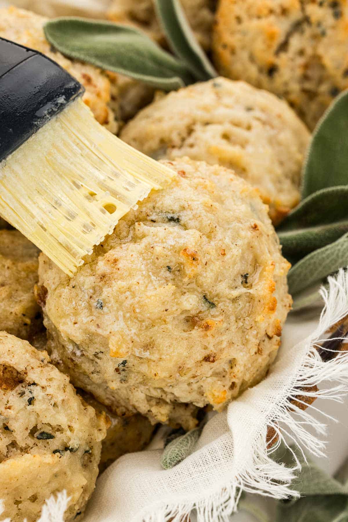 Closeup of a biscuit getting brushed with butter.
