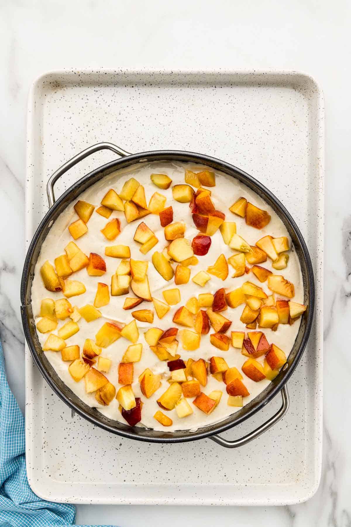 Peach chunks pressed into the top of a pan of cheesecake batter.