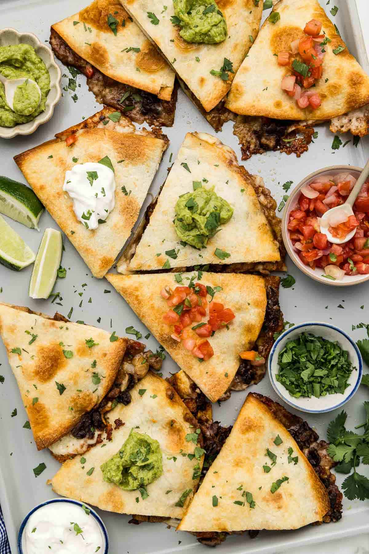 Sliced quesadillas topped with a variety of condiments on a large sheet pan.