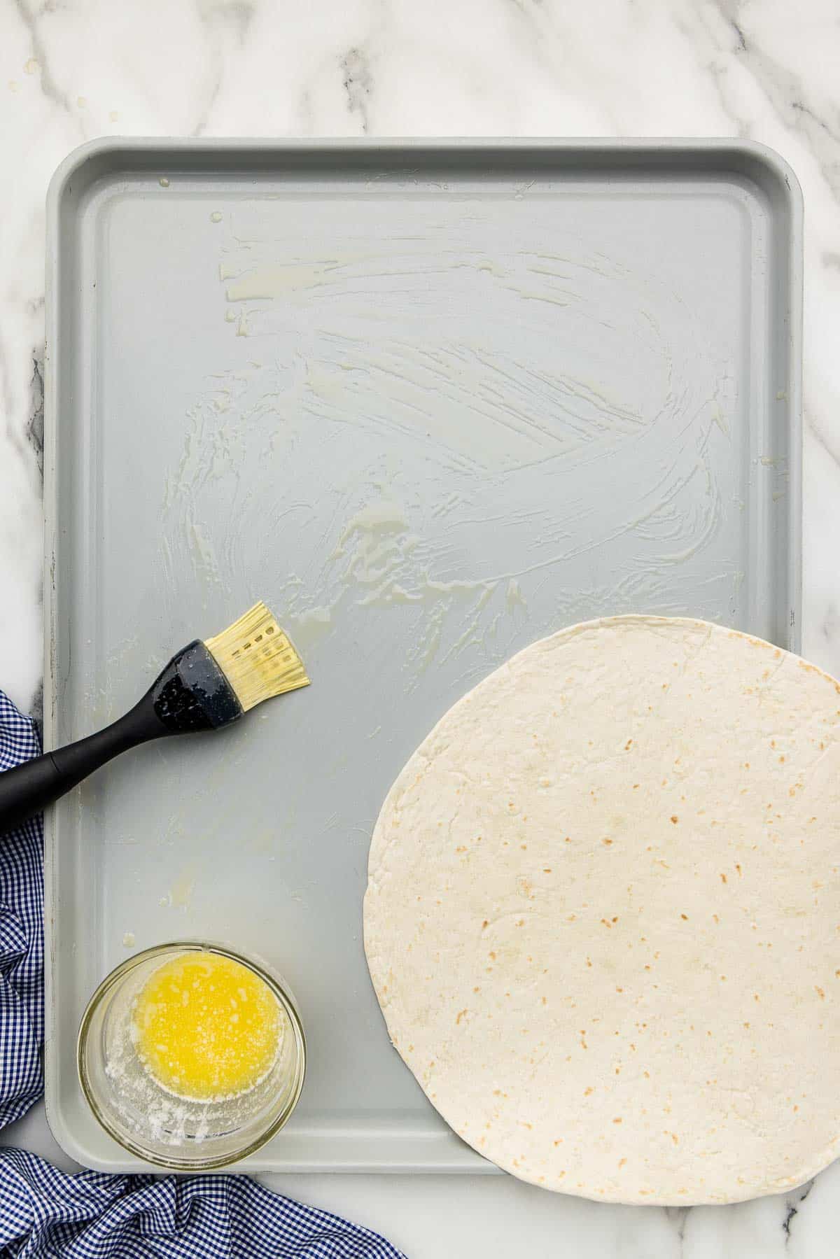 A cooking pan brushed with a buttered silicone brush with a tortilla laid over the corner.