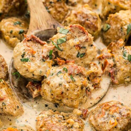 A cooking spoon scooping up a handful of meatballs.