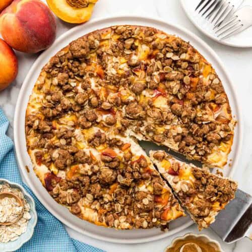 Overhead of a peach cheesecake with a slice being taken out.