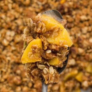 Closeup of a spoon holding a bite of peach crumble.