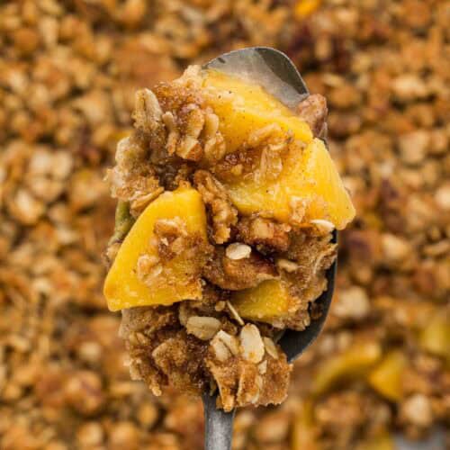 Closeup of a spoon holding a bite of peach crumble.
