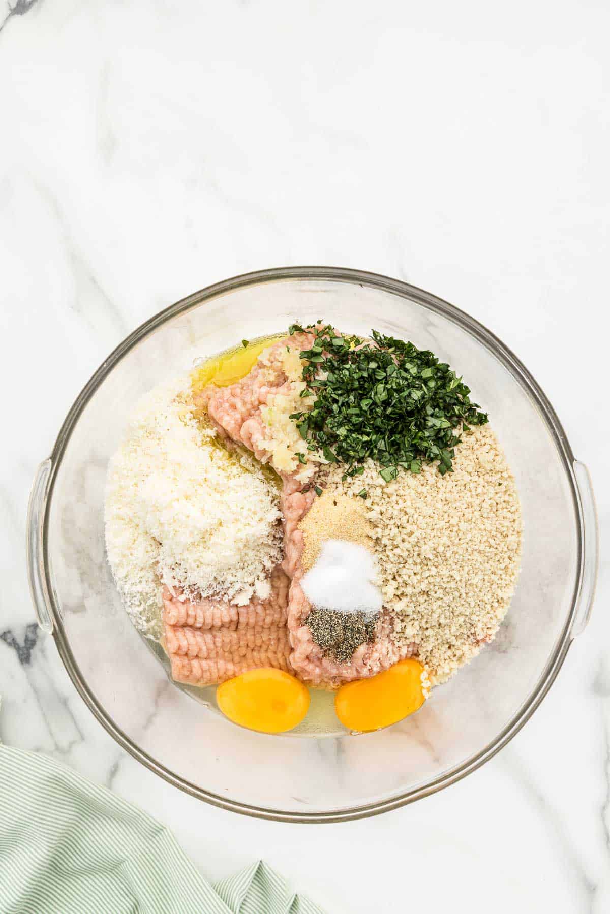 Chicken meatballs ingredients unmixed in a glass bowl.