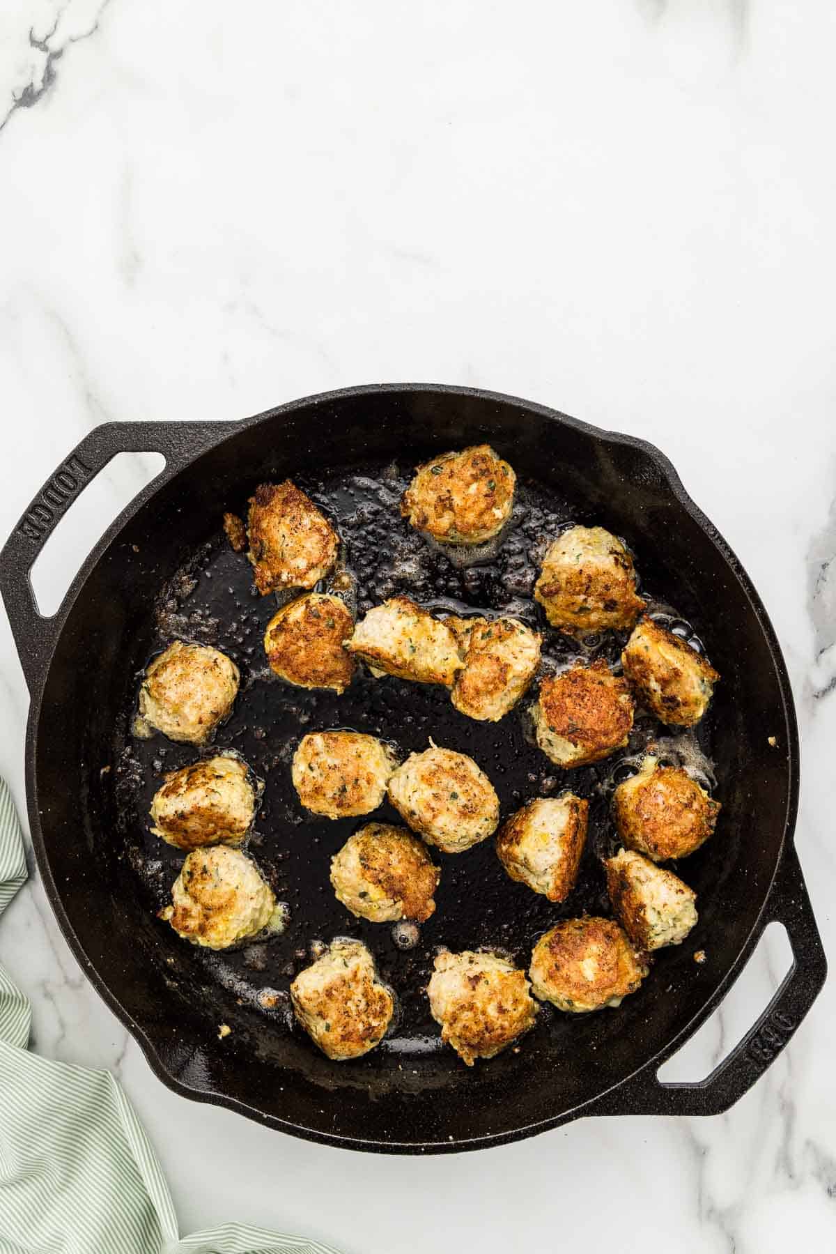 A cast iron skillet with cooking chicken meatballs.