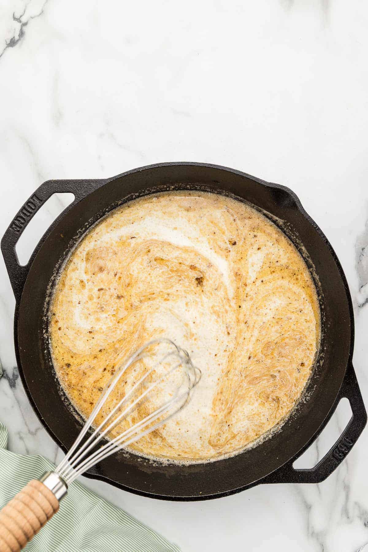 Creamy sauce stirred in a skillet with a whisk.
