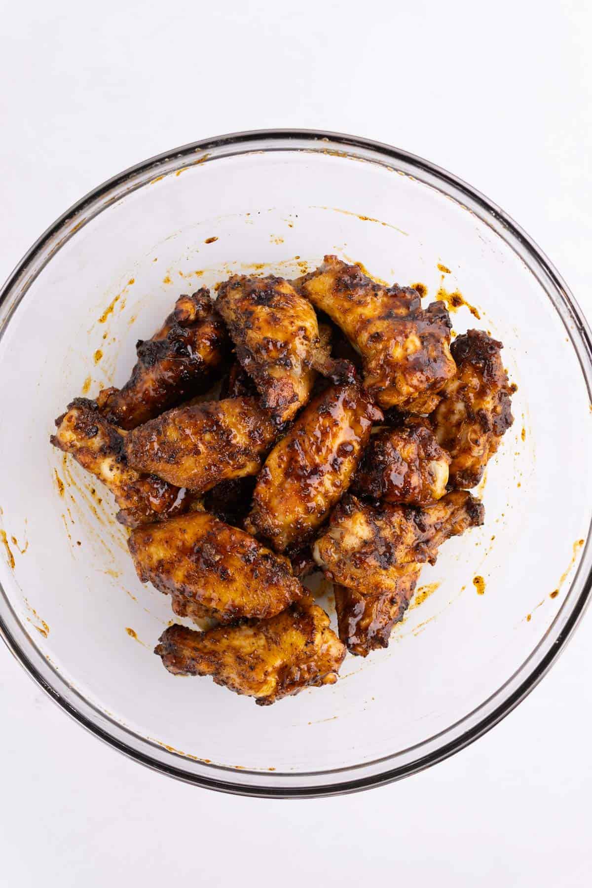 Grilled chicken wings in a glass bowl covered in sauce.